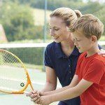 Female Tennis Coach Giving Lesson To Boy